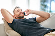 © peopleimages.com - Relax, smile and phone call with man on sofa for communication, good news and contact. Happiness, calm and technology with male person in living room of home for mobile, digital and networking