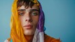 Close-up Portrait of Young Man with Blue Eyes Wrapped in Colorful Scarf Against Blue Background - Non-Binary person
