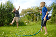 Funny little boy with his father playing with garden hose in sunny backyard. Preschooler child having fun with spray of water. Summer vacation in the village for family with kids.