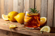 Iced tea or alcoholic cocktail with ice, rosemary and lemon slices on a old wooden table.