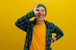 Excited young Asian man, wearing a beanie hat and casual shirt, is making an OK gesture with his hand positioned as if using binoculars, with his eyes peering through the opening formed by his fingers