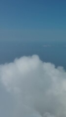 Wall Mural - Flying through beautiful white fluffy clouds in sky over blue sea. Airplane travel background. Vertical video