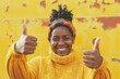 Cheerful young woman in yellow sweater and headwrap smiling and showing thumbs up with both hands