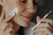 © DK_2020 - A woman applying a medicated cream on one side of her face as part of an acne treatment routine