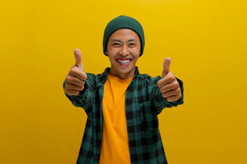 A smiling young Asian man, dressed in casual clothes and wearing a beanie hat, is giving a thumbs up gesture, indicating a positive or good review while standing against a yellow background