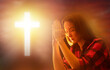 Woman praying to god. Catholic girl sits with folded palms. Praying lady near cross. Catholic crucifix at sunset. Orthodox cross. Religious woman praying. Female turns to god with eyes closed