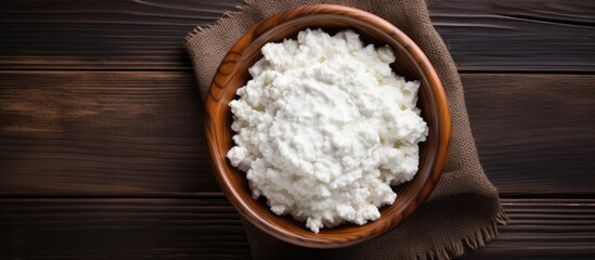 A top down view of cottage cheese in a wooden bowl accompanied by sour cream set against an old wooden background providing ample copy space for your text