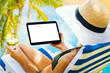 woman holding digital tablet with blank screen while laying down on beach chair at resort. mockup