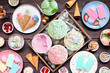 Cool summer food table scene. Assortment of ice cream, popsicles and frozen treats. Pastel colors. Top down view on a dark wood background.