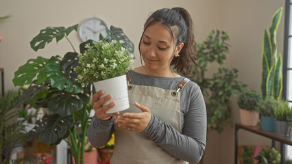 Sticker - A young hispanic woman admires a potted plant inside a verdant flower shop with various greenery in the background.