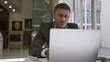 © Krakenimages.com - Focused african man working on a laptop in a modern office, portraying professionalism and determination.