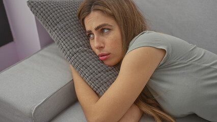 Canvas Print - A beautiful, contemplative young caucasian woman lounges indoors, her gaze distant, resting thoughtfully on a sofa pillow.