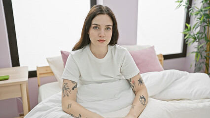 Poster - A casual young woman with tattoos sits calmly on a bed in a brightly lit, modern bedroom