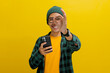 An Asian man, donning a beanie hat, casual shirt, and eyeglasses, flashes an OK sign towards the camera while holding a phone, conveying satisfaction, approval and a positive review, yellow background