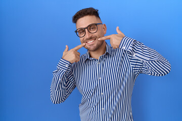 Poster - Hispanic man with beard wearing glasses smiling cheerful showing and pointing with fingers teeth and mouth. dental health concept.