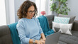 © Krakenimages.com - Hispanic woman with curly hair working on laptop in home living room with decorative pillows and plants.