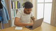© Krakenimages.com - Focused black man using laptop in a cozy home office setup with books and personal decor.