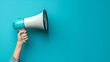 © P - A hand is shown holding a megaphone against an blue background, symbolizing communication or announcement. The image is dynamic and attention-grabbing, with copy space
