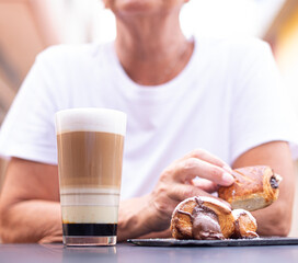 Wall Mural - Unrecognizable senior woman sitting at cafe table in the morning having breakfast with sweet food and milk and coffee