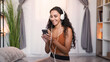 Music app. Phone playlist. Gadget entertainment. Relaxed smiling woman in headphones enjoying listening to song at light modern home interior with free space.