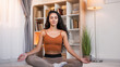 Meditation practice. Yoga relaxation. Peaceful smiling girl enjoying calming exercise sitting cross-legged in lotus pose on floor at light home interior with copy space.