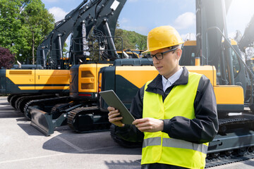 Aufkleber - Engineer in a helmet with a digital tablet stands next to construction excavators