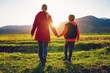 Mother and son walking through a picturesque mountain valley at sunset holding hands, back view