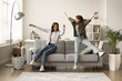 Cheerful mom and excited teenager kid hitting couch at home, jumping, flying in air, throwing bodies on soft comfortable sofa, screaming, laughing, having fun, playing active games, Full length