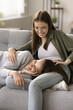 Cheerful pretty teenager daughter cuddling young mom lying on sofa with love, care, laughing. Young mother and kid enjoying close trustful relationships, friendship, affection, leisure. Vertical shot
