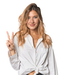 Wall Mural - Caucasian blonde woman in studio showing victory sign and smiling broadly.