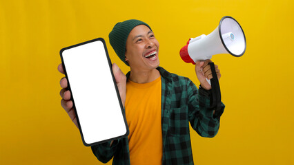 Excited Asian man shows a phone with an empty blank screen for copy space while holding a megaphone to announce a discount sale, special offer, or promote a new app. Isolated on a yellow background