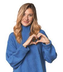 Wall Mural - Caucasian blonde woman in studio smiling and showing a heart shape with hands.