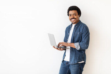 Poster - African American man is standing, holding a laptop in his hands. He is looking at the screen intently, possibly working or browsing. The background is white with copy space