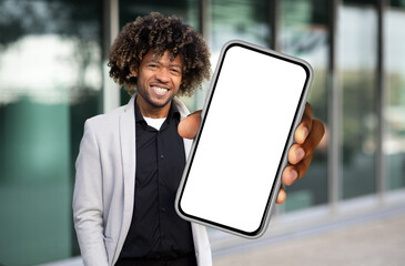 Poster - African American man is standing while holding a cell phone in his hand, looking at the screen. He appears focused and engaged with the device, possibly texting or browsing.