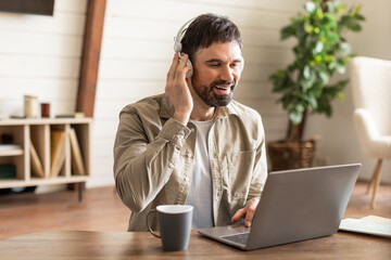 Aufkleber - A man is seated at a table, focused on his laptop screen while wearing headphones. He appears to be working or studying intently.