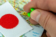 Travel to Japan. A hand inserting a pin to mark the direction of the trip, an embroidered Japanese flag. Vacation or business travel concept.