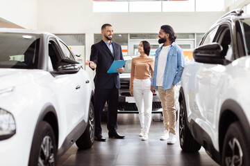 a well-dressed salesman is presenting information to indian couple in a car dealership showroom. the