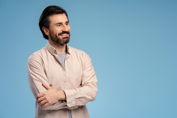 Wall Mural - Smiling bearded young man holding arms crossed, posing in studio. Copy space. Advertisement concept