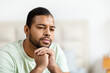 © Prostock-studio - African American man appears deep in thought as he rests his chin on his hand, his gaze slightly off-camera. His facial expression conveys contemplation or concern, copy space