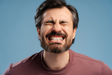 Wall Mural - Young man screw up his eyes while posing in studio and showing his tooth, isolated on blue