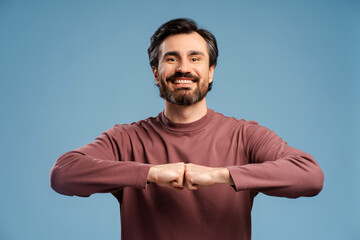 Wall Mural - Happy young man showing fists bump gesture posing in studio, isolated on blue background