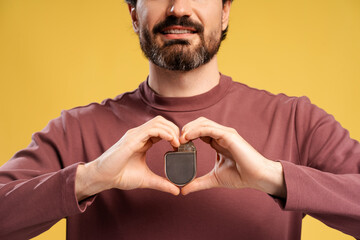 Wall Mural - Portrait of young man showing pacemaker in two hands, isolated in yellow background