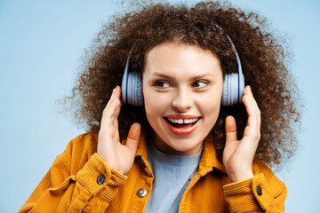 Woman with curly hair wearing stylish yellow jacket listening to music in wireless headphones