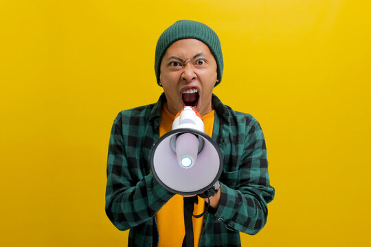 young asian man in a beanie hat and casual shirt shouts through a megaphone, expressing annoyance an