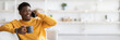 © Prostock-studio - Cheerful black guy in yellow sitting on sofa, having phone conversation with friend and laughing, holding mug with coffee, looking at copy space. Handsome millennial black man spending weekend at home