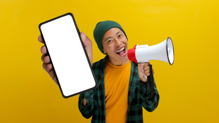 Excited Asian man shows a phone with an empty blank screen for copy space while holding a megaphone to announce a discount sale, special offer, or promote a new app. Isolated on a yellow background