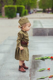 Fototapeta  - Adorable baby in Soviet military uniform lays a flower on a monument