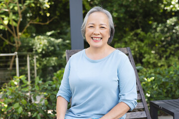 Wall Mural - Asian senior female sitting outdoors, smiling at camera