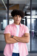 In modern office, a young biracial male coworker standing with arms crossed