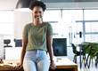 © Wavebreak Media - At office, African American businesswoman sitting on desk, smiling at camera
